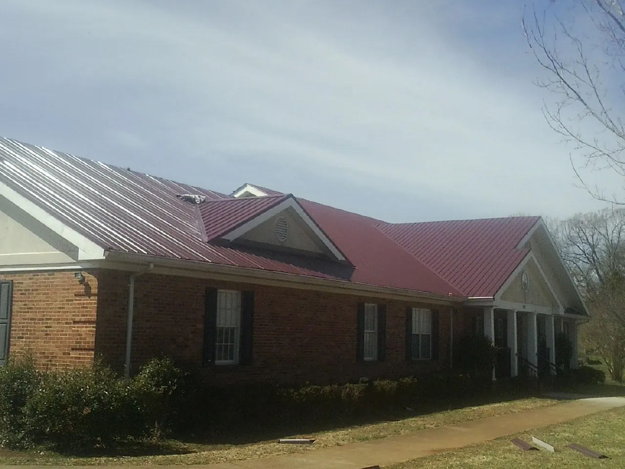 Red metal roof with gabled entries on a long brick building, from a Hail Damage Roof Repair job in Spreckels